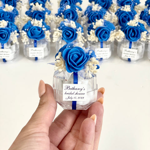 Hand holding a small decorative bottle with blue flowers against a background of similar bottles.