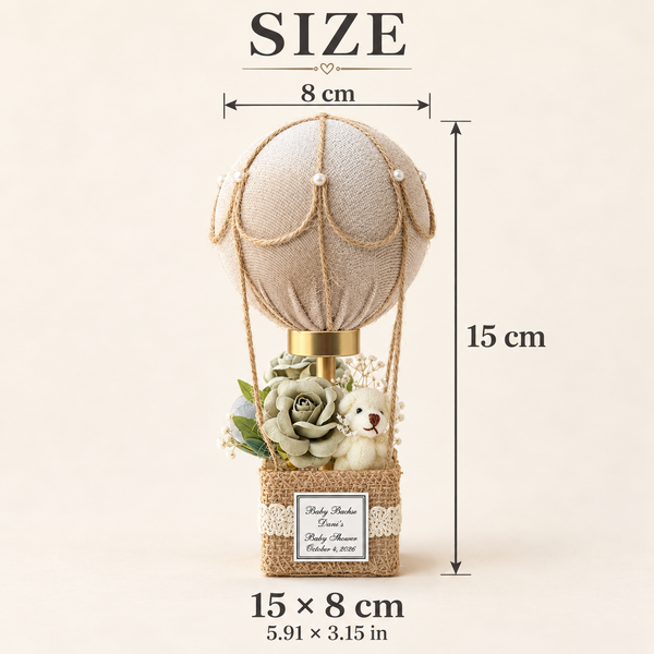A decorative hot air balloon figurine with a beige fabric balloon, rope details, a burlap basket base, faux flowers, and a small plush bear. The image includes size annotations showing 15 cm height, 8 cm width, and overall 15 x 8 cm dimensions on a plain light beige background.