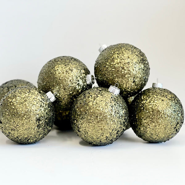 A group of seven glittery gold Christmas baubles with silver hanging loops, arranged on a plain white surface against a white background.