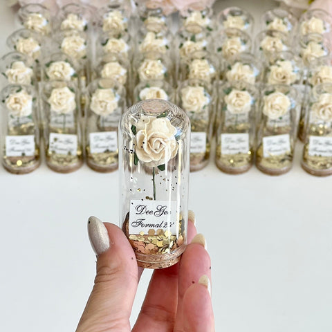 Small glass bottle with a preserved flower held by a hand, with more bottles in the background.