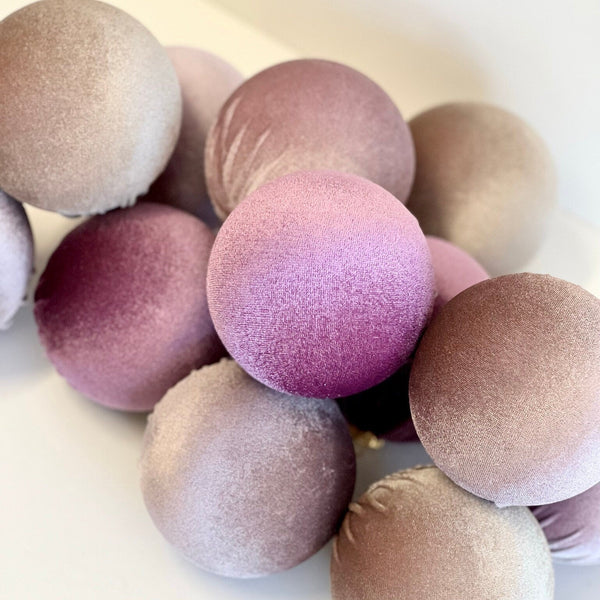 A cluster of velvet decorative spheres in muted dusty pink, mauve, taupe, and lavender tones, photographed on a clean white surface.