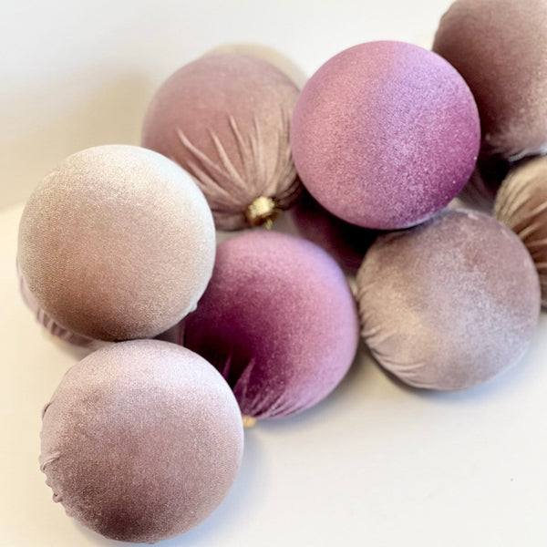 A cluster of velvet decorative ornaments in muted shades of mauve, dusty rose, and taupe on a plain light background.