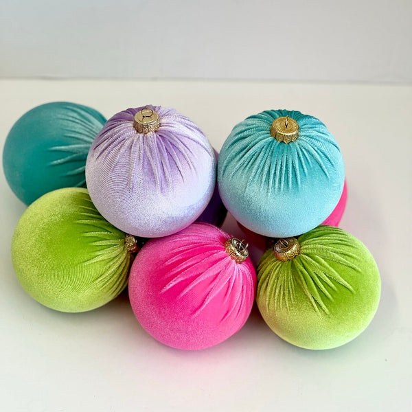 A group of six velvet Christmas tree ornaments in assorted bright colors including pink, green, blue, and purple, arranged on a plain white surface.