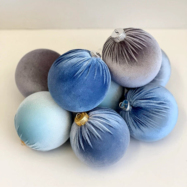 A pile of velvet Christmas ornaments in shades of blue, gray, and lavender, with one ornament featuring a small gold cap.