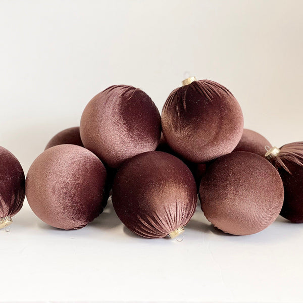 A group of velvet Christmas ornaments in a deep plum-brown color, arranged on a plain white studio background.