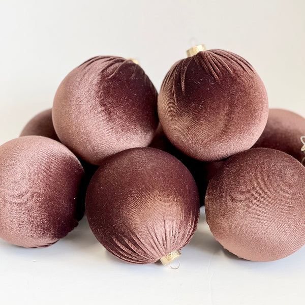 A pile of round velvet Christmas ornaments in a dusty rose or mauve color, photographed on a clean white background.