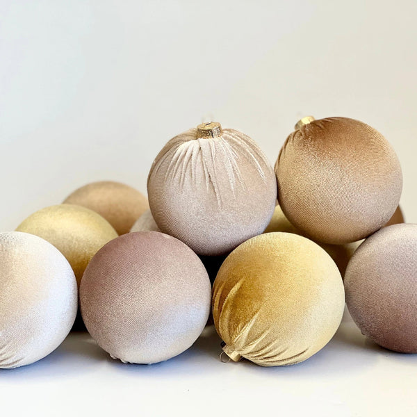 A group of velvet Christmas tree ornaments in soft neutral shades including beige, gold, bronze, and dusty rose, arranged on a clean white background.