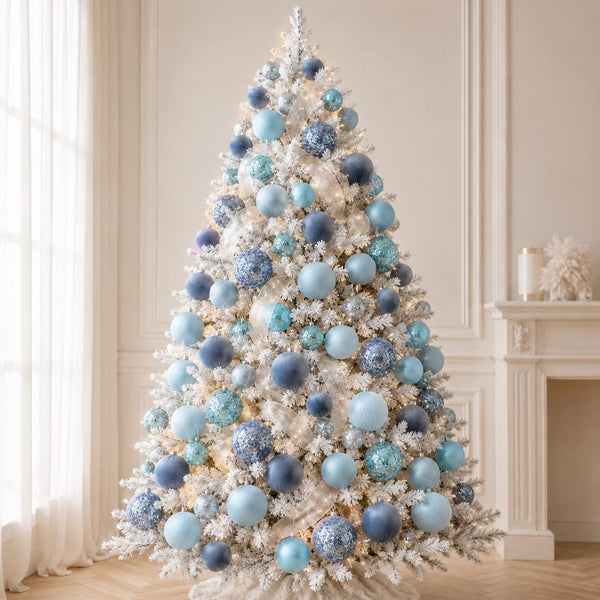 A white flocked Christmas tree decorated with light blue, navy, and white ornaments, set in a bright, elegant room with a fireplace and sheer curtains.